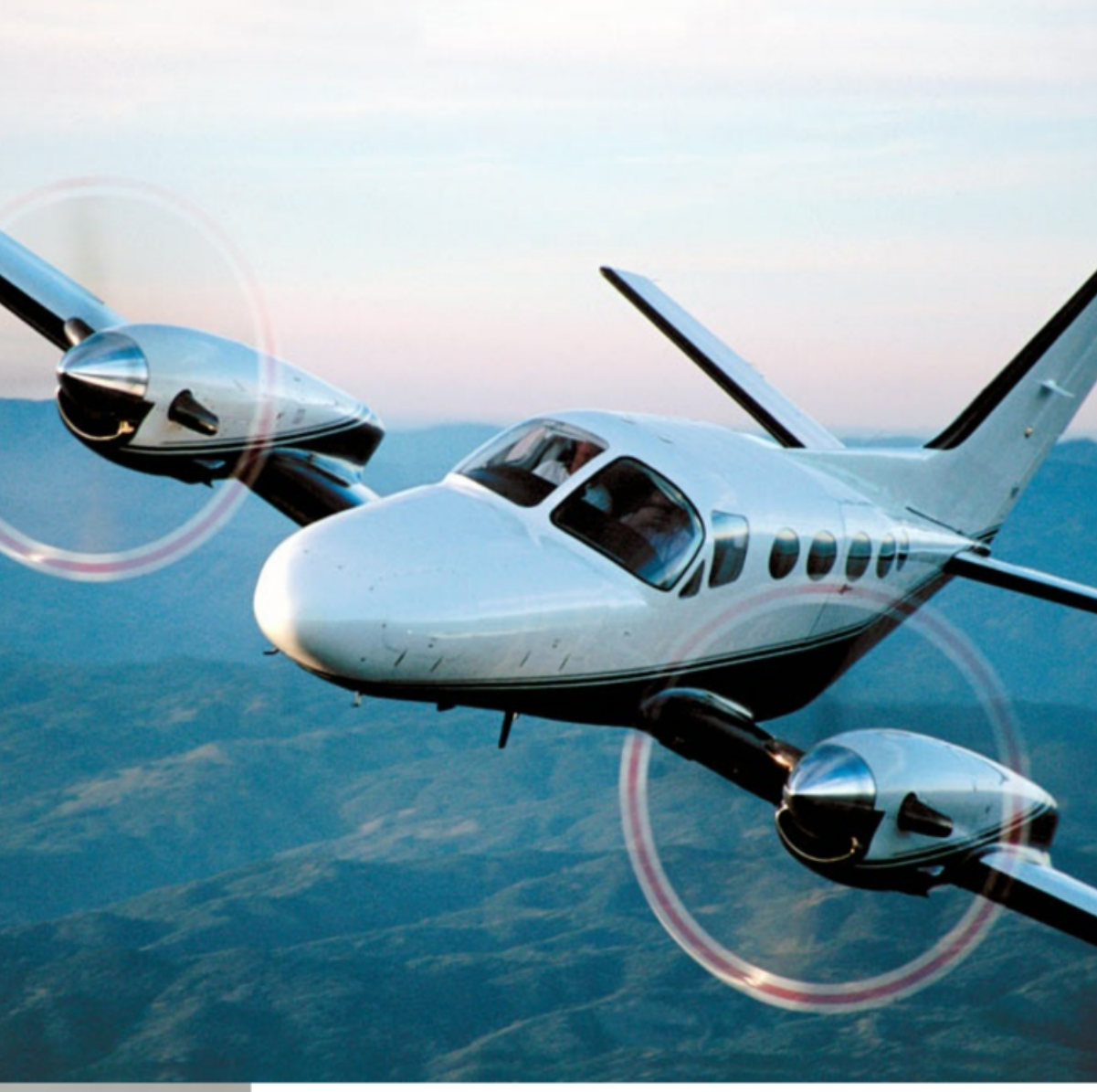 A twin-propeller executive aircraft in flight over mountainous terrain